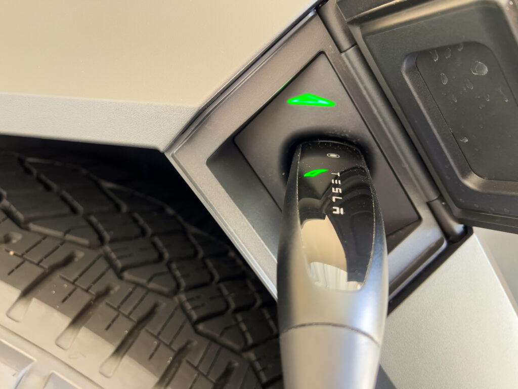 A close-up of an electric vehicle being charged, showing the charging cable plugged in with a glowing green indicator light.